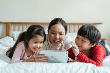 a boy and girl with female caregiver looking at a tablet device together