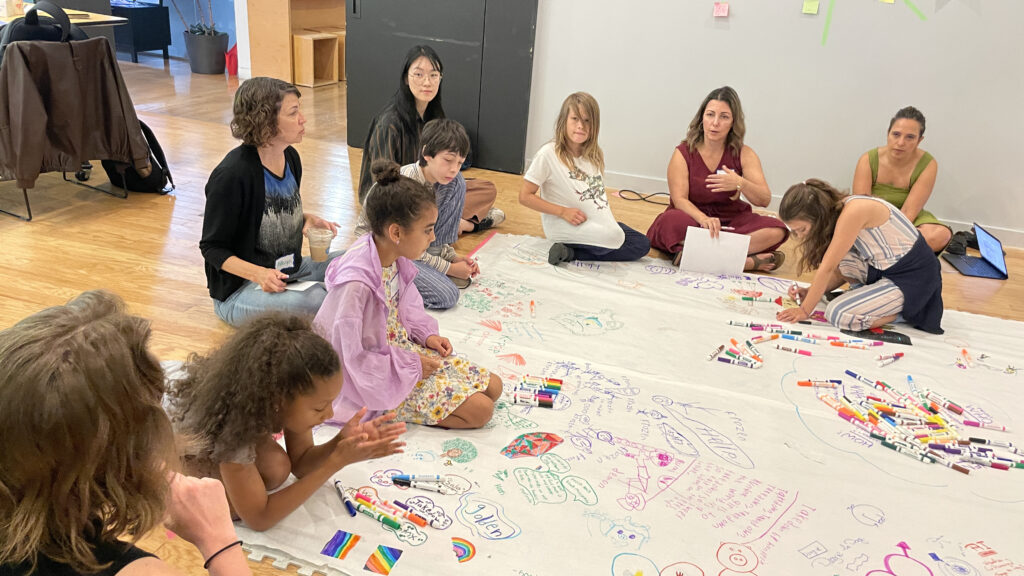 Students and adults sit on the floor at a co-design session.